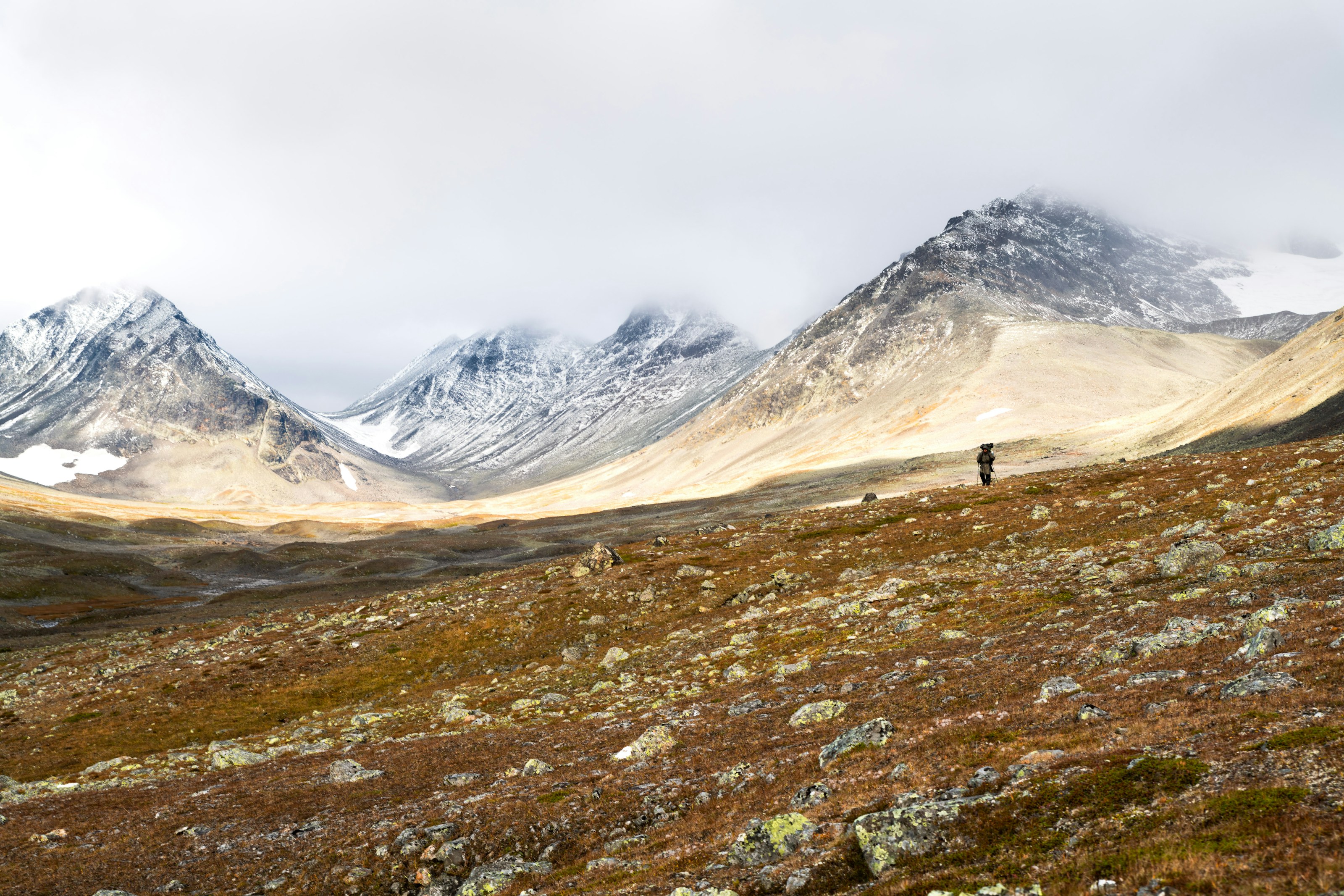 A lone figure crossing high autumn tundra beneath snow-dusted peaks in Sarek National Park